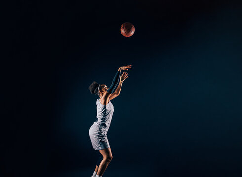 Side view of a basketball woman throwing a ball up in the studio