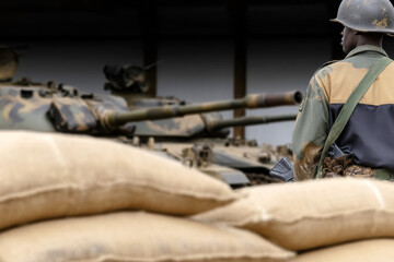 Obraz premium A soldier in camouflage uniform stands guard near military tanks and sandbags, showcasing military preparedness and defense