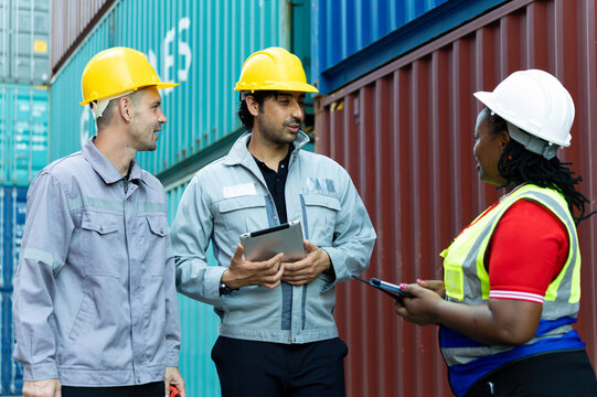 Multinational logistics workers discussing shipment operations at container yard, using digital tablet for cargo management, teamwork, industrial communication and global supply chain coordination