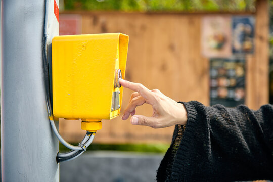 Close-up of hand pressing outdoor emergency button on yellow control box, symbolizing public safety system, emergency response access, security technology and instant alert communication in urban
