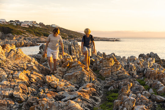 2 pre teen boys climbing and exploring rocky coastline of DeKelders, South Africa