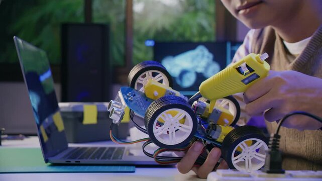 Asian teenager doing Arduino robot homework project in house, technology of robotics programing and kids education concept.