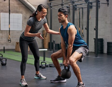 Southeast Asian personal trainer guides client through functional strength exercise in modern gym atmosphere