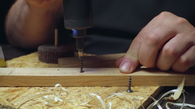 Skilled craftsman uses electric screwdriver to fasten screws into wooden plank, showcasing detailed woodworking process in a workshop environment
