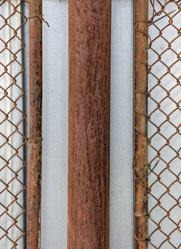 Symmetrical rusty metal pillar and wire fence on industrial background