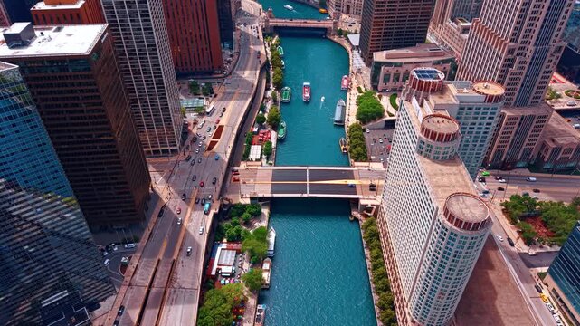 Vessels move by the blue waterscape of the Chicago River. Cars go by the highways along the river and across it. Chicago, Illinois, USA. Aerial view.