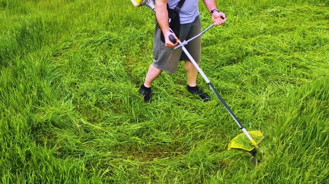 Experience a tranquil summer moment, where a male worker diligently uses a petrol lawn mower trimmer. The freshly cut grass glistens, merging nature with the art of landscaping.