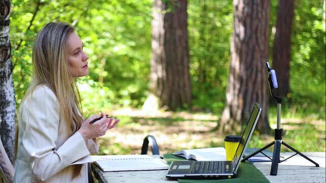 A charming woman conducts an insightful online consultation in the embrace of nature. Her warm demeanor and expert guidance create a memorable atmosphere for all involved. Slow motion 4k video.