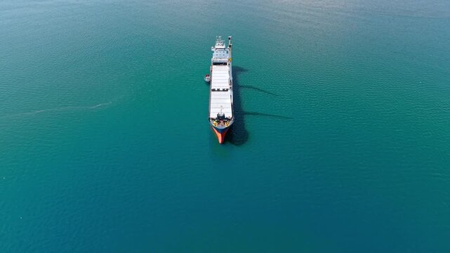 Overhead view on the huge cargo ship standing on the vast turquoise waterscape. Freight vessel on the roadstead.