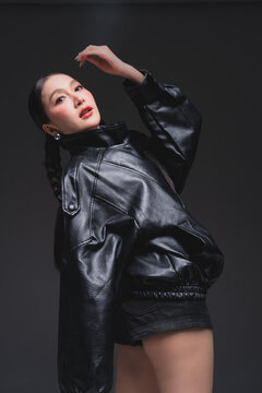 Side profile of Asian woman looking over shoulder in leather jacket for high fashion cosmetics marketing campaign luxury streetwear aesthetic urban lifestyle edgy portrait studio