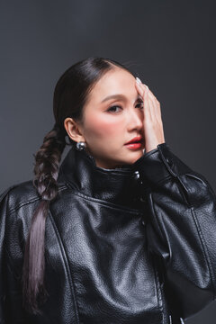 Mysterious Asian woman covering half face in leather jacket for high fashion cosmetics skincare marketing campaign intense eye contact dualism concept edgy portrait studio