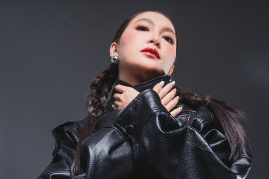 Low angle of confident Asian woman in leather jacket for high fashion cosmetics marketing campaign luxury streetwear aesthetic female empowerment concept edgy portrait studio