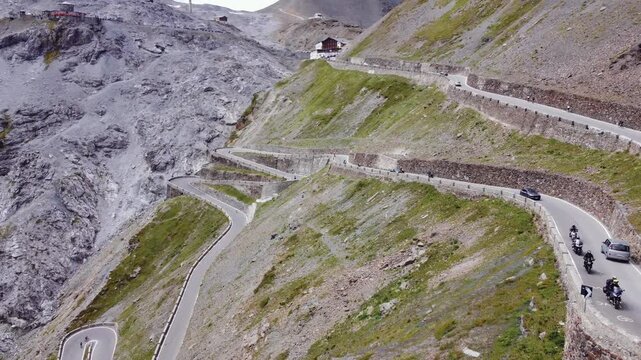 Aerial 4K drone footage of the majestic Stelvio Pass in the Italian Alps, showing the famous winding serpentine road carved into a dramatic, rugged mountain landscape and high alpine peaks.