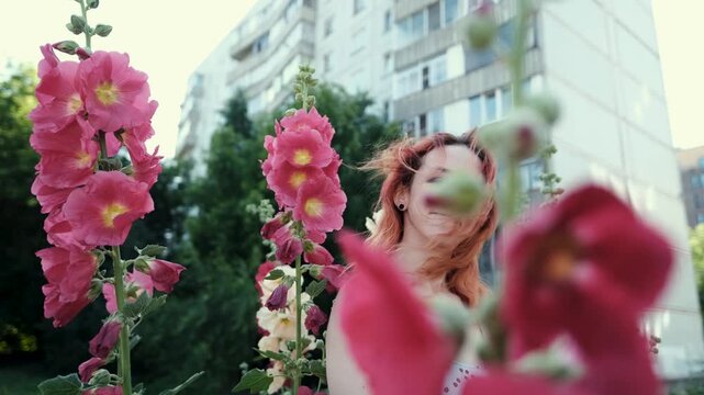Young girl smiling, breathing, relaxing against the background of pink blooming mallow flowers, allergy health concept: spring, blooming flowers, allergy, health