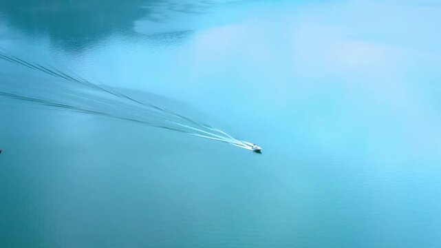 Aerial view of speedboat cruising on calm blue lake near small rocky islet