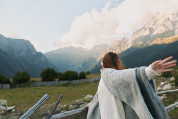 A woman stands outdoors with arms outstretched, facing mountains and a sunlit landscape, conveying freedom, joy, and a relaxed lifestyle in nature. © SHOTPRIME STUDIO