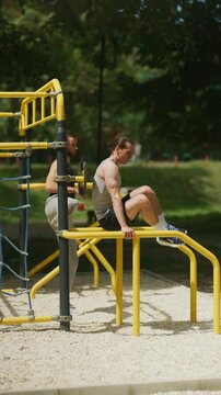 Muscular men perform bodyweight exercises on yellow parallel bars at an outdoor calisthenics park. Two athletes engage in strength training, focusing on fitness and muscle development in a sunny park
