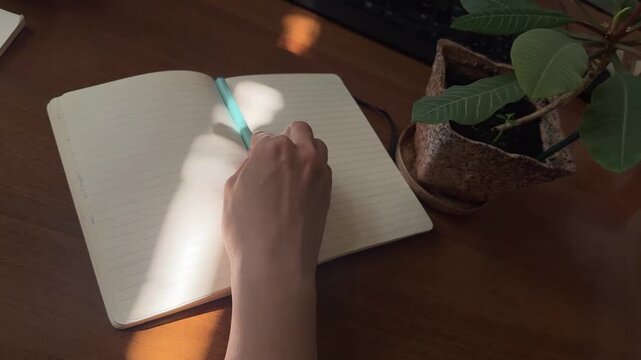 Hand moving pen across open notebook under shifting sunlight