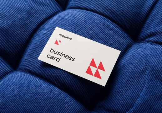 High-angle shot of a blank business card mockup resting on a blue tufted corduroy velvet fabric texture