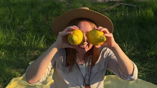 Woman in sun hat holding lemons over eyes moving in garden