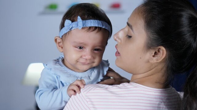 A smiling Indian mother soothing her unhappy little daughter - young parent  crying baby. Closeup shot of a female babysitter holding a sweet infant in her arms  - family bonding  work flexibility ...