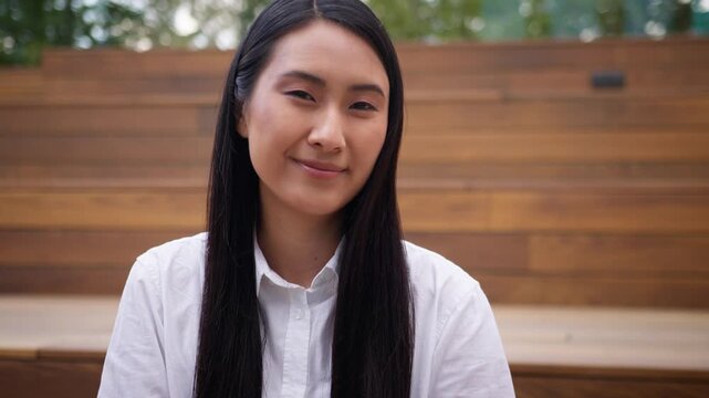 Pensive smiling Asian Korean Chinese business woman looking at camera calm smile in city Japanese female businesswoman girl worker manager posing outside in downtown happy agent employer lady portrait