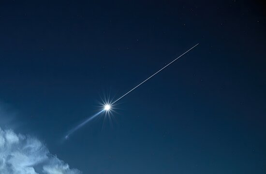 Bright celestial object trails across dark night sky with wispy clouds