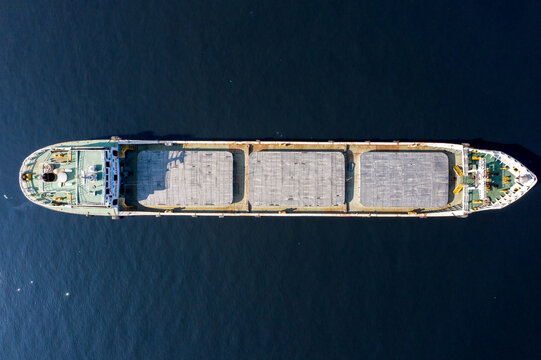 Aerial view of a large cargo ship with three hatches navigating the dark blue waters of the Shitalakkha River in Gazipur District, Dhaka Division, Bangladesh.
