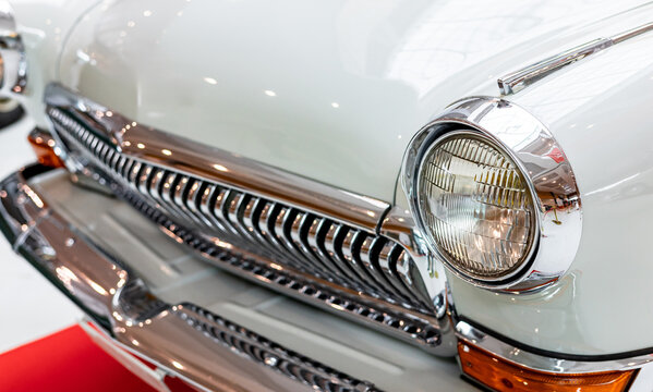Close-up of the round headlamps of a white classic car. Beautifully restored chrome details of a historic vehicle. Round headlight of a white old timer car
