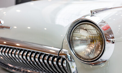 Close-up of the round headlamps of a white classic car. Beautifully restored chrome details of a historic vehicle. Round headlight of a white old timer car © NastyaPhoto