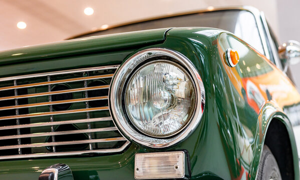 Close-up of the round headlights of a green classic car. Beautifully restored chrome parts of a historic vehicle. Round headlight of a green vintage car.