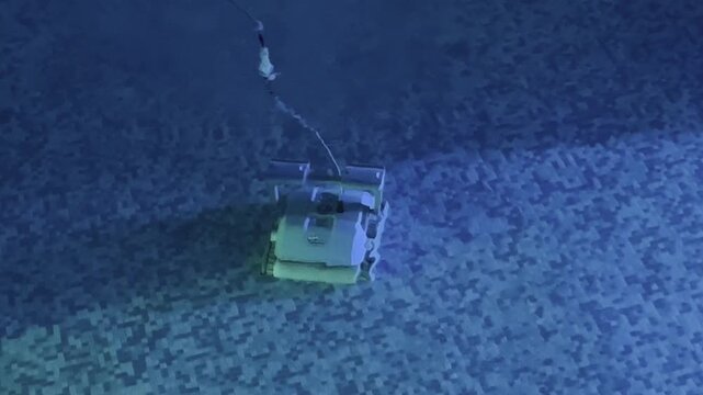 Close up robotic pool cleaner moving on swimming pool floor with mosaic tiles and blue green underwater lighting during automatic pool cleaning. High quality 4k footage