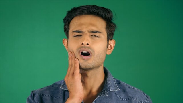 Handsome Indian guy with a toothache. Green screen / Chroma shoot. An attractive Indian man touching his cheeks because of toothache - doctor  dental cavity  unhealthy lifestyle