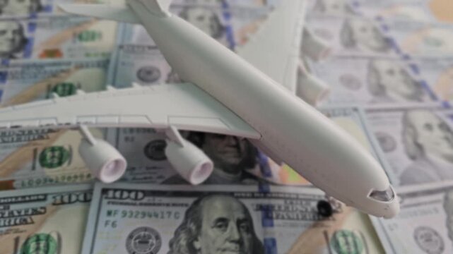 Model airplane placed on a pile of hundred dollar bills in a flat lay setup