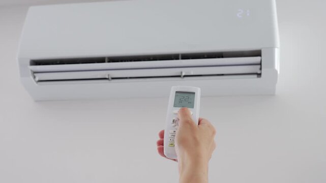 Hand sets a comfortable temperature on a wall air conditioner with a remote control indoors. Concept of room cooling, climate control and indoor comfort.