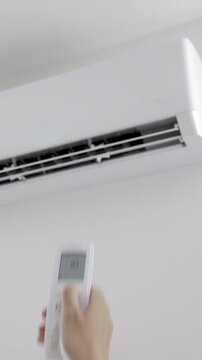 Hand using remote control to adjust temperature on wall mounted air conditioner in modern room. Concept of home cooling, indoor climate control and summer comfort