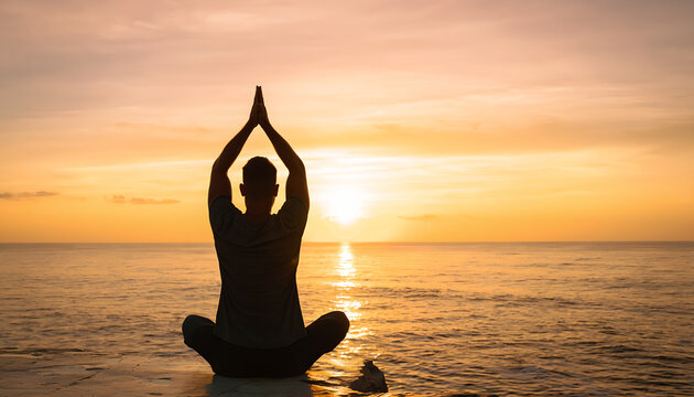Man practicing yoga meditation in lotus position on beach at beautiful sunset silhouette view