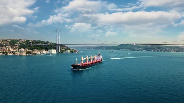 Large bulk carrier cargo ship navigating through Bosphorus Strait under famous suspension bridge with Ortakoy Mosque in Istanbul, Turkey