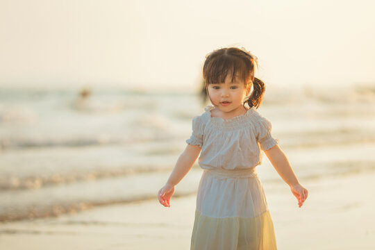 Cute little Asian girl walking on sandy beach at sunset, happy child enjoying tropical sea view during golden hour, family travel vacation, outdoor learning, active childhood growth and parenting