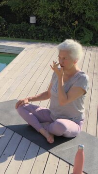 Vertical video: Holding nose, senior in tee breathing, stretching for calm on deck with pink bottle