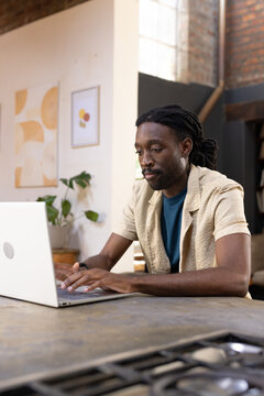 African man sitting at kitchen island typing on silver laptop in open-plan loft studio