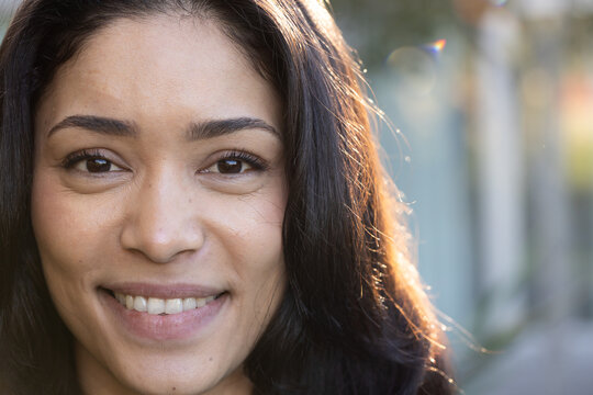 Woman in 30s smiling, turning toward warm rim sunlight on pathway with lens flare bokeh