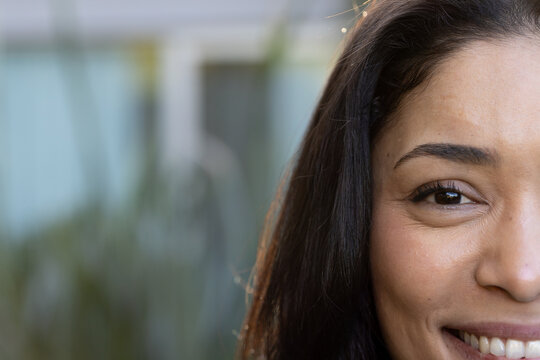 African woman smiling, turning toward camera on balcony with blurred plants and railing, copy space