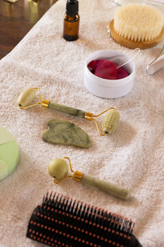 Green stone rollers are resting on beige towel over wood table, surrounded by brush and jar