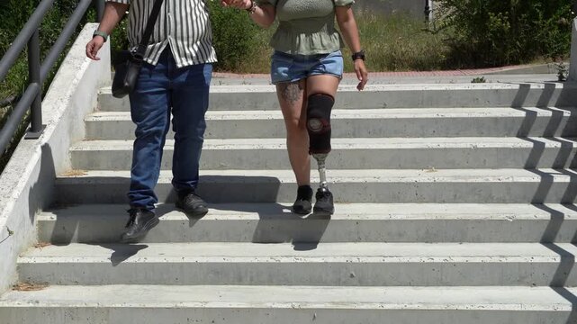 Young couple holding hands while walking down concrete stairs. The woman has a below-the-knee prosthetic leg, symbolizing resilience and love