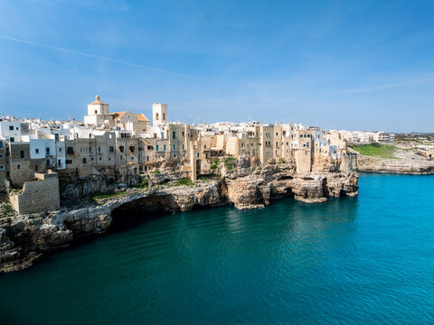 Aerial view of the historic white buildings perched on limestone cliffs above the turquoise Adriatic Sea in Polignano a Mare, Apulia, Italy.
