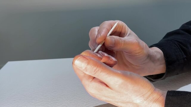 Man holds a wood cuticle stick over a finger nail in closeup. Self grooming, care, manicure treatment at home.