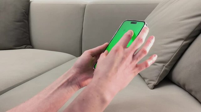 Hands hold smartphone with green screen and perform pinch zoom gesture on display. Fingers enlarge image on chroma interface at home. Concept touch interaction, mobile control, digital usage