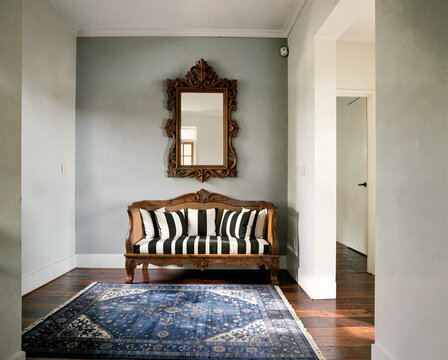 Elegant wooden bench with striped cushions under ornate mirror in stylish hallway with blue rug.