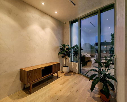 Modern minimalist living room with wooden furniture, indoor plants, and large glass windows overlooking urban evening view